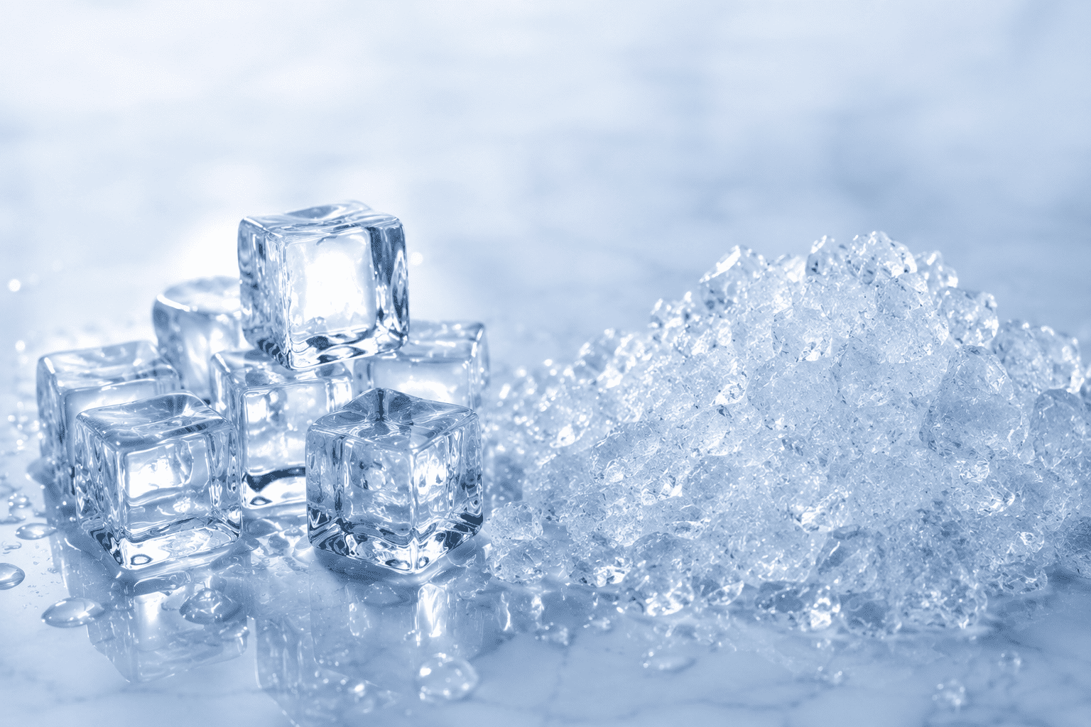 Cluster of transparent ice cubes stacked beside a pile of crushed ice on a reflective surface.